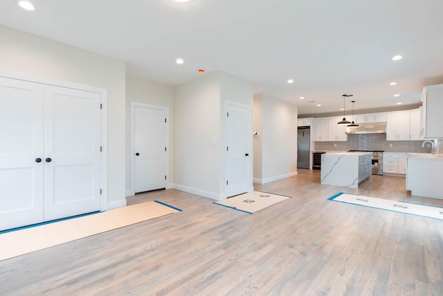unfurnished living room with baseboards, recessed lighting, light wood finished floors, and a sink