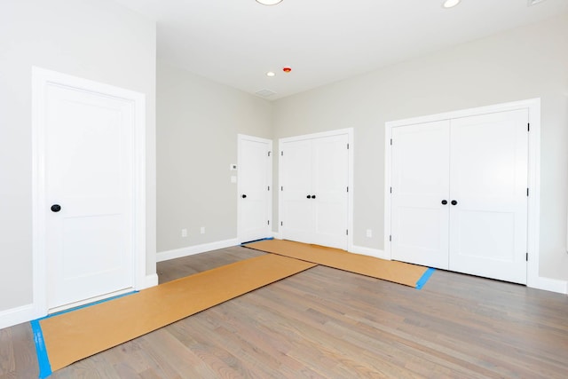 unfurnished bedroom featuring two closets, wood finished floors, baseboards, and recessed lighting