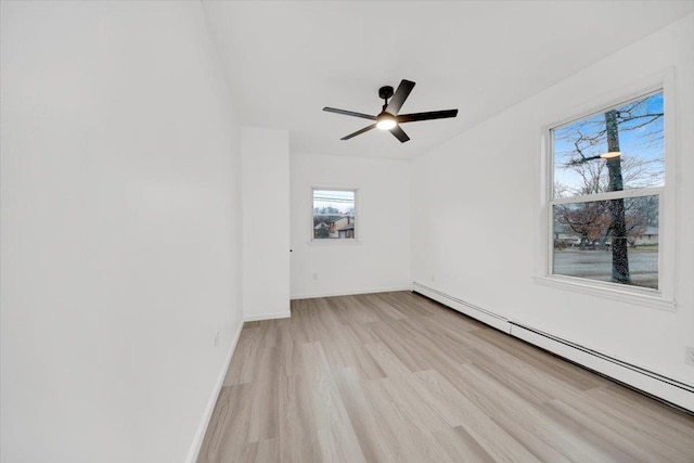 spare room featuring a ceiling fan, light wood finished floors, baseboards, and a baseboard heating unit