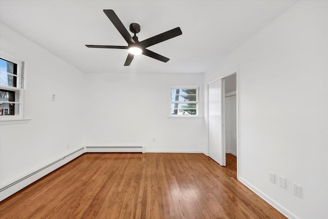 unfurnished bedroom featuring a closet, baseboards, wood finished floors, and a baseboard heating unit