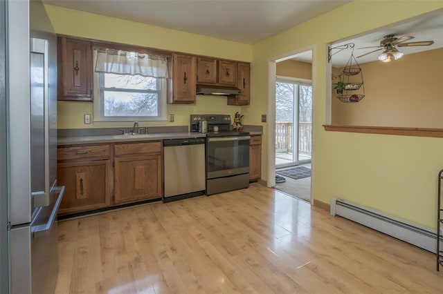 kitchen featuring brown cabinets, appliances with stainless steel finishes, under cabinet range hood, a sink, and a baseboard heating unit