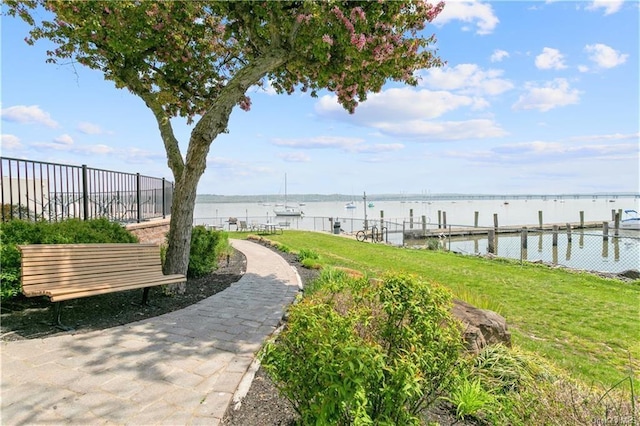 view of dock featuring a lawn, fence, and a water view