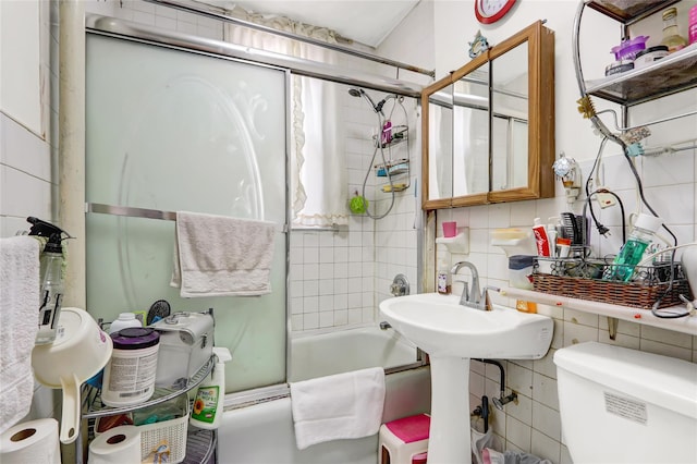 bathroom featuring toilet, a sink, enclosed tub / shower combo, decorative backsplash, and tile walls
