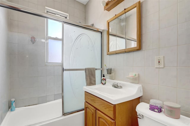 bathroom with toilet, vanity, combined bath / shower with glass door, and tile walls