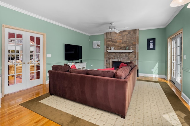 living area with crown molding, wood finished floors, a stone fireplace, ceiling fan, and french doors