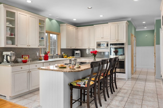 kitchen featuring a kitchen bar, crown molding, appliances with stainless steel finishes, a sink, and marble finish floor
