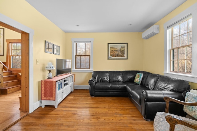 living room with plenty of natural light, stairway, a wall mounted AC, and light wood-type flooring