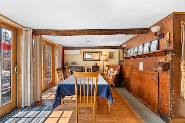 dining room featuring an AC wall unit, a healthy amount of sunlight, wood finished floors, and beam ceiling