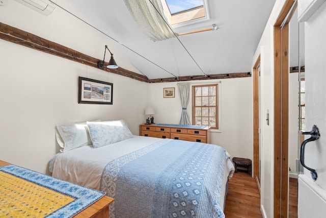 bedroom featuring baseboards, vaulted ceiling with skylight, and wood finished floors