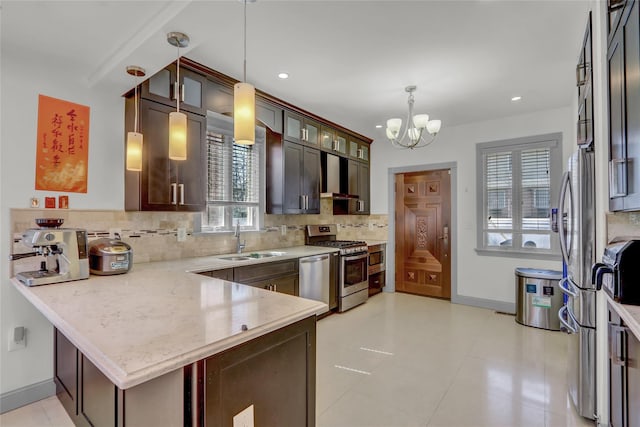kitchen featuring a chandelier, backsplash, a sink, a peninsula, and appliances with stainless steel finishes