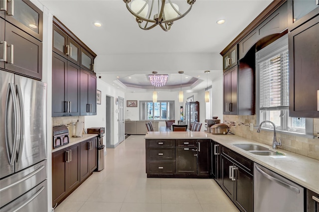 kitchen featuring light countertops, a chandelier, a raised ceiling, a sink, and appliances with stainless steel finishes