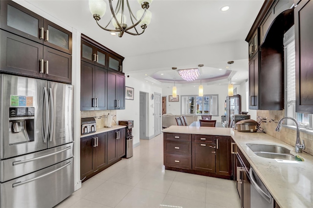 kitchen featuring appliances with stainless steel finishes, a sink, a tray ceiling, backsplash, and a notable chandelier