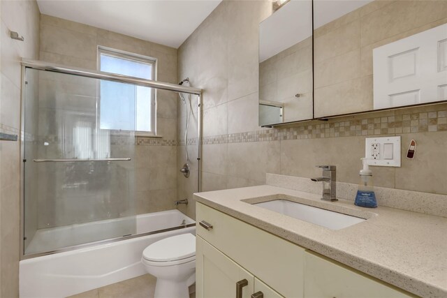 full bath with tile walls, combined bath / shower with glass door, toilet, vanity, and tasteful backsplash