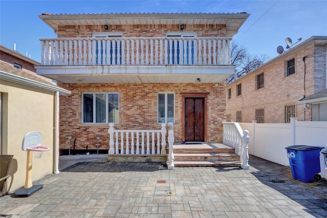 back of property featuring a balcony, fence, and brick siding