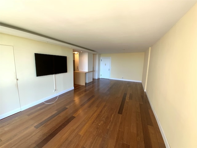 unfurnished living room with dark wood-type flooring and baseboards