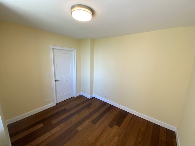 empty room featuring baseboards and dark wood-type flooring