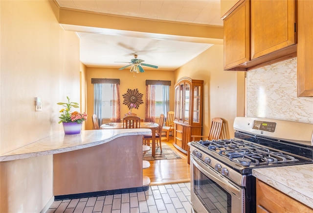 675 N Oakwood Rd, Laurel, NY 11948 - kitchen featuring a ceiling fan, tasteful backsplash, brown cabinetry, stainless steel gas stove, and light countertops