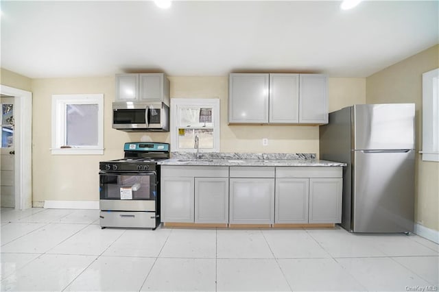 kitchen with baseboards, appliances with stainless steel finishes, a sink, gray cabinetry, and light tile patterned floors