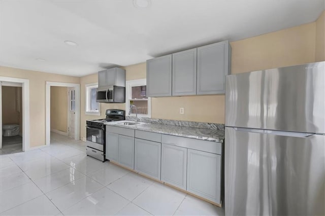 kitchen featuring gray cabinetry, a sink, light tile patterned flooring, and appliances with stainless steel finishes