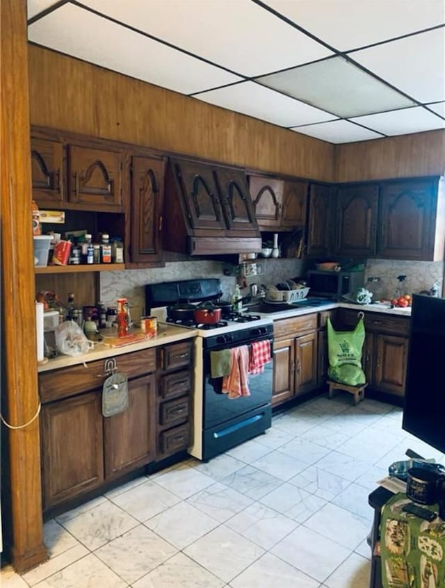 kitchen featuring backsplash, light countertops, stainless steel microwave, and gas range