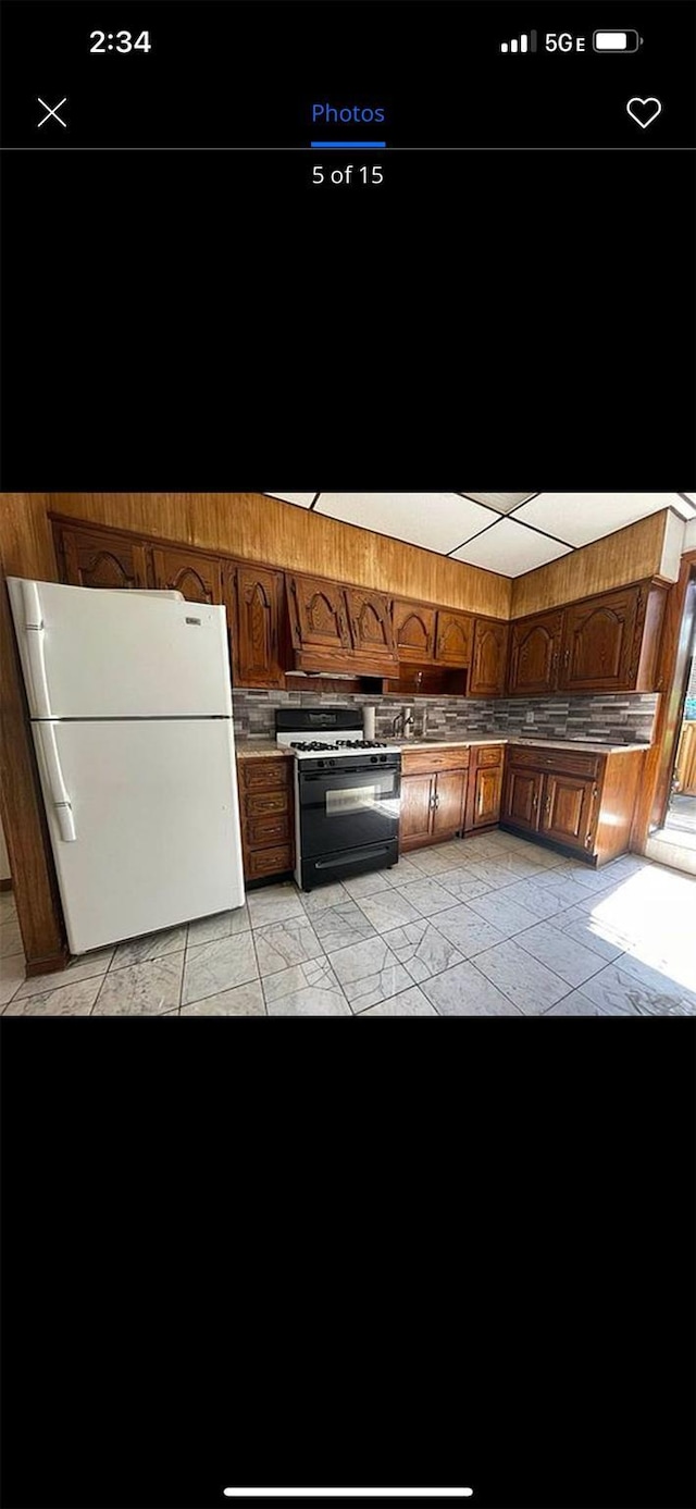 kitchen featuring gas range, brown cabinetry, wooden walls, and freestanding refrigerator