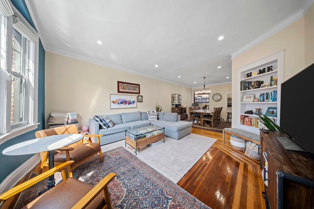living area featuring hardwood / wood-style floors, ornamental molding, built in features, and a healthy amount of sunlight