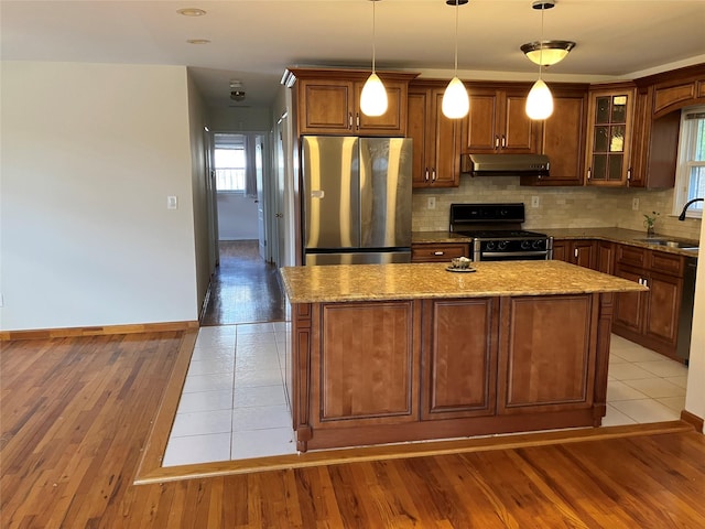 kitchen featuring a kitchen island, tasteful backsplash, appliances with stainless steel finishes, under cabinet range hood, and light stone counters