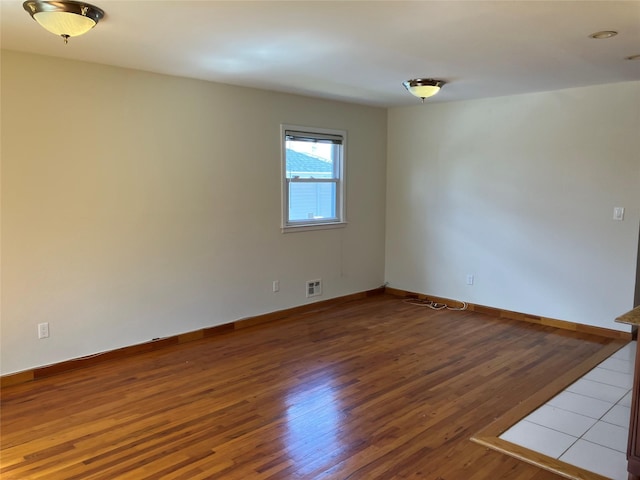 empty room featuring wood finished floors, baseboards, and visible vents