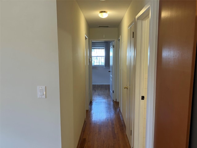 hall with baseboards, visible vents, and dark wood finished floors
