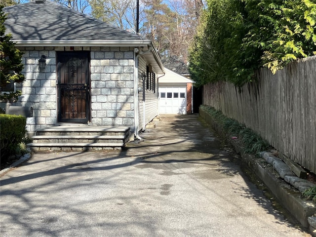 view of property exterior with stone siding, roof with shingles, an outbuilding, fence, and a garage