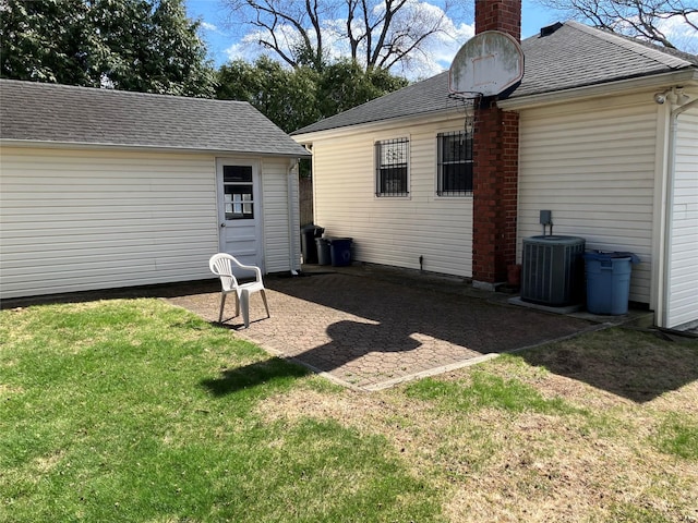 back of house with a chimney, roof with shingles, a lawn, cooling unit, and a patio area