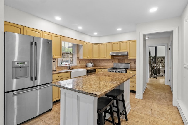 kitchen with stainless steel appliances, under cabinet range hood, decorative backsplash, a kitchen island, and a sink