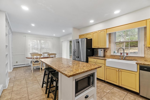 kitchen with a kitchen breakfast bar, stainless steel appliances, decorative backsplash, a sink, and light stone counters
