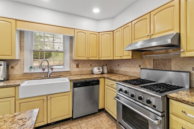 kitchen featuring under cabinet range hood, backsplash, a sink, light stone countertops, and appliances with stainless steel finishes