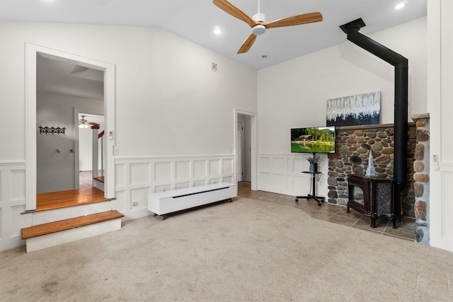 interior space with vaulted ceiling, ceiling fan, a decorative wall, and a wood stove