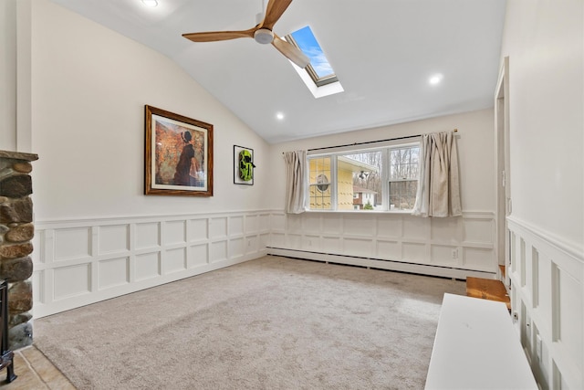 carpeted spare room featuring a baseboard heating unit, recessed lighting, lofted ceiling with skylight, a ceiling fan, and wainscoting