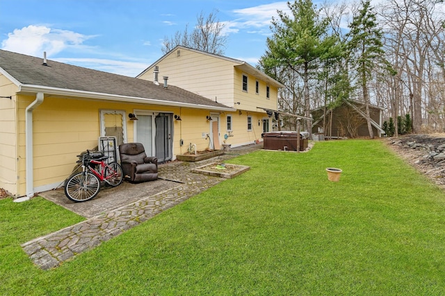 rear view of property featuring a hot tub, a shingled roof, and a lawn