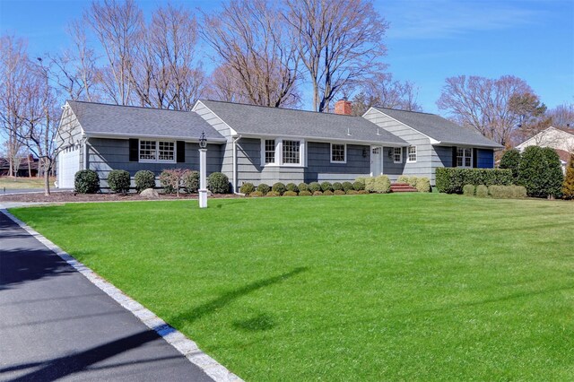 single story home featuring an attached garage, a chimney, a shingled roof, and a front yard