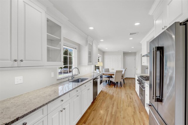 kitchen with light wood finished floors, glass insert cabinets, white cabinetry, a sink, and high quality appliances