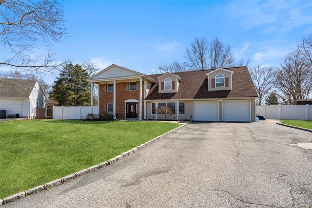 greek revival inspired property featuring a front yard, fence, a garage, and aphalt driveway