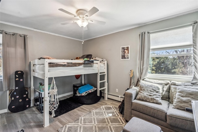 bedroom featuring baseboards, crown molding, wood finished floors, and a baseboard heating unit