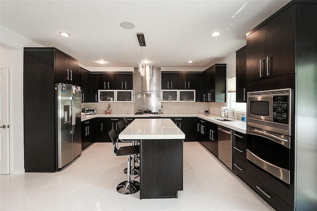 kitchen with stainless steel appliances, wall chimney range hood, a breakfast bar area, light countertops, and decorative backsplash