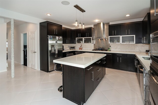 kitchen featuring stainless steel appliances, wall chimney exhaust hood, a center island, decorative backsplash, and light countertops