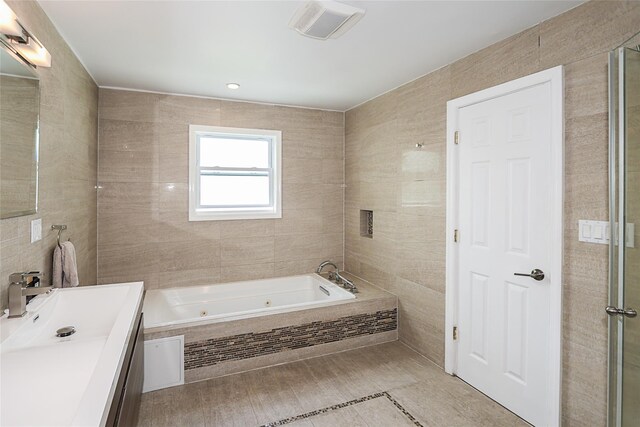 bathroom with tile walls, a tub with jets, vanity, and tiled shower