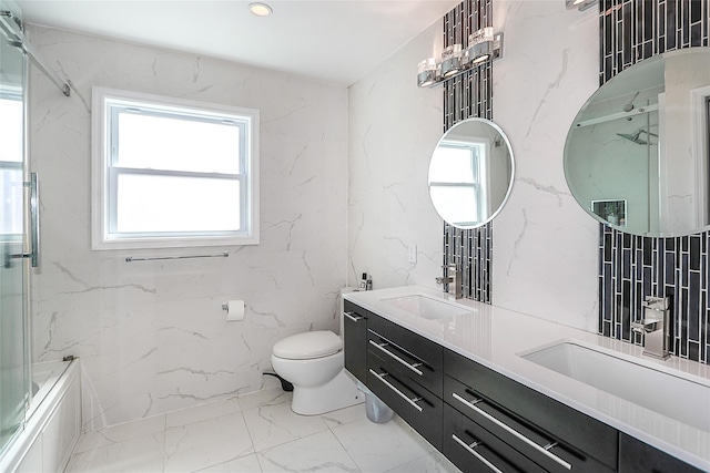 bathroom featuring toilet, marble finish flooring, double vanity, stone wall, and combined bath / shower with glass door