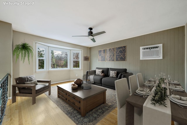 living room featuring a wall mounted AC, light wood-style floors, baseboards, and a ceiling fan