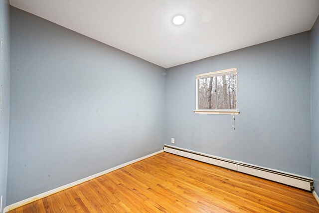 empty room with baseboards, wood finished floors, and baseboard heating