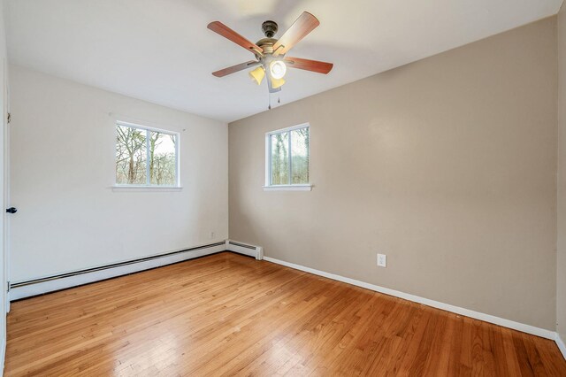 spare room featuring a baseboard heating unit, baseboards, a ceiling fan, and hardwood / wood-style floors