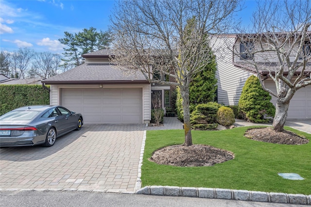 traditional-style home featuring a shingled roof, decorative driveway, a garage, and a front lawn