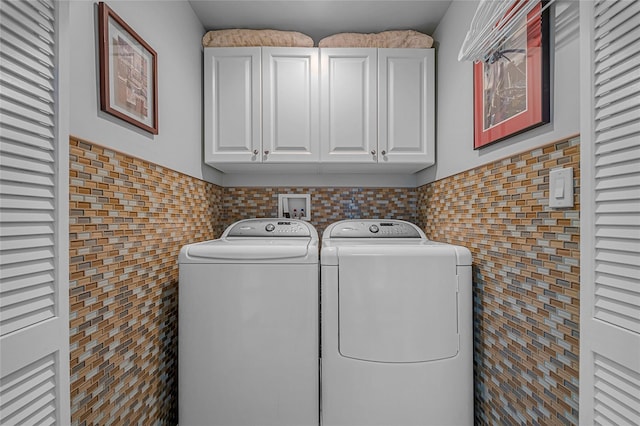 laundry area featuring a wainscoted wall, washing machine and clothes dryer, cabinet space, and tile walls